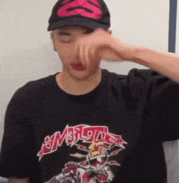 a man wearing a hat and a t-shirt is covering his face .