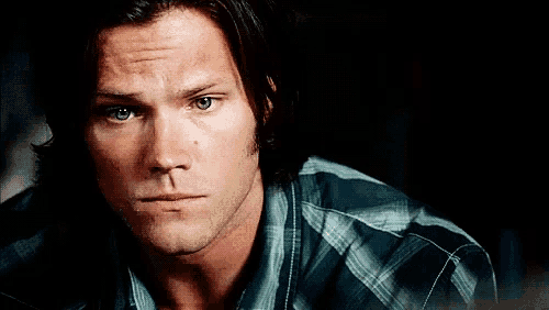 a man with long hair is wearing a plaid shirt and looking at the camera
