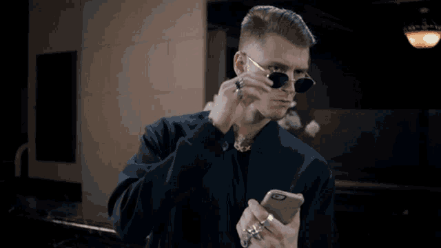 a man wearing sunglasses and a ring is looking at his phone