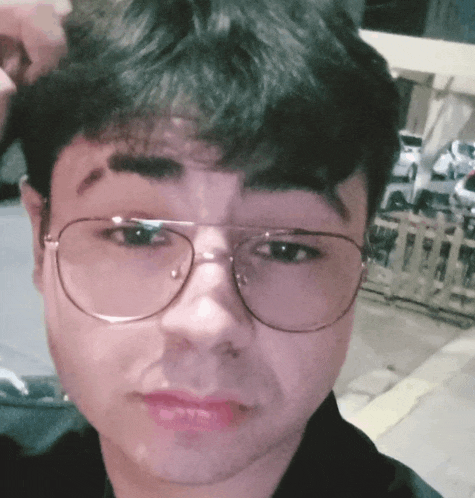 a young man wearing glasses and a black shirt looks at the camera