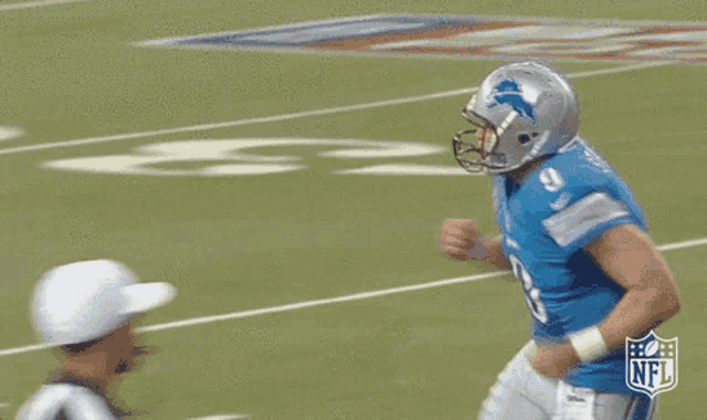a football player wearing a helmet and a blue shirt is running on a field .