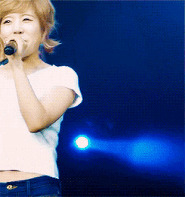 a woman is singing into a microphone in front of a blue light