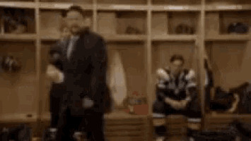a man in a suit and tie is standing in a locker room .