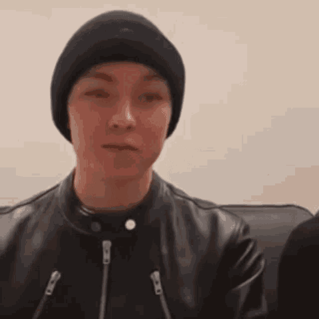 a young man wearing a black beanie and a leather jacket .