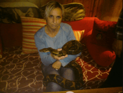 a woman sits on a couch holding a snake in her hands