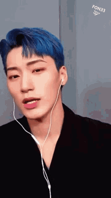 a young man with blue hair is wearing earphones and a black jacket .