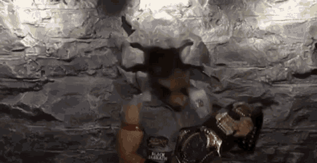 a man in a cowboy hat is holding a wrestling championship belt in front of a rock wall .