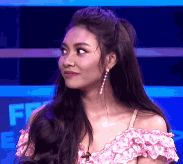 a woman wearing a pink off the shoulder top and earrings looks at the camera .