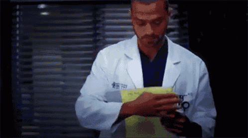 a man in a lab coat is standing in front of a window holding a piece of paper .