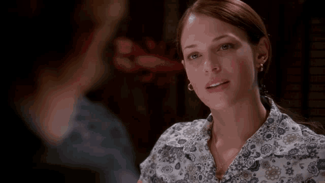 a woman wearing a floral shirt and earrings smiles at a man