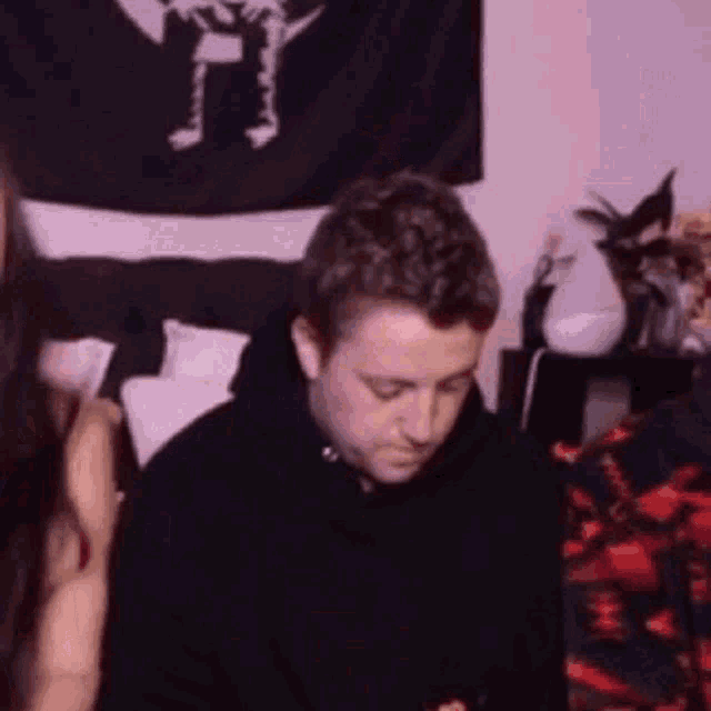 a man in a black hoodie is sitting next to a woman in a room .