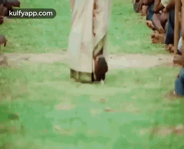 a man is walking on a green field in front of a crowd of people .