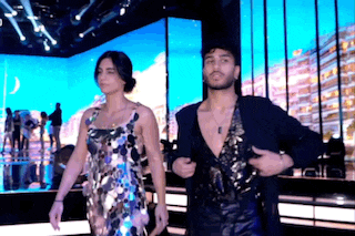 a man and a woman are standing next to each other on a stage . the woman is wearing a sequined dress .