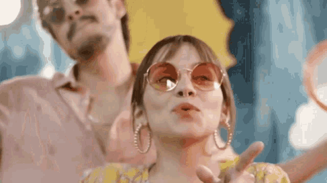a man and a woman are standing next to each other wearing sunglasses and making a peace sign .
