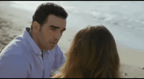 a man and a woman are sitting on a beach looking at each other