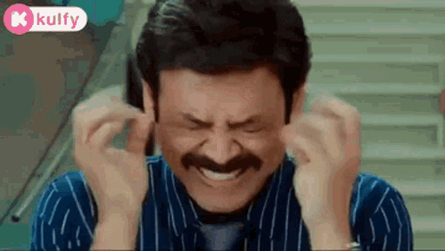 a man with a mustache is covering his ears with his hands and laughing .