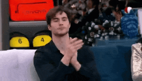 a man is clapping his hands while sitting on a couch in front of a table .