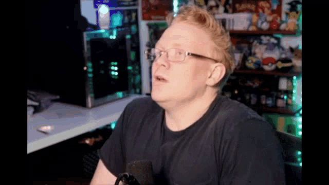 a man with glasses is sitting in front of a microphone in a room .