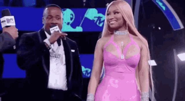 a woman in a pink dress is standing next to a man in a suit holding a microphone on a stage .
