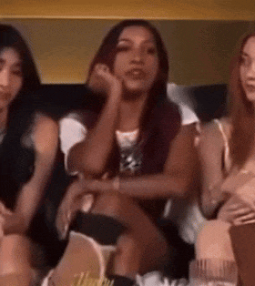 three women are sitting on a couch with their legs crossed and their hands on their faces .
