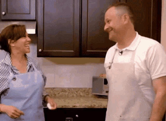 a man and a woman wearing aprons are smiling in a kitchen
