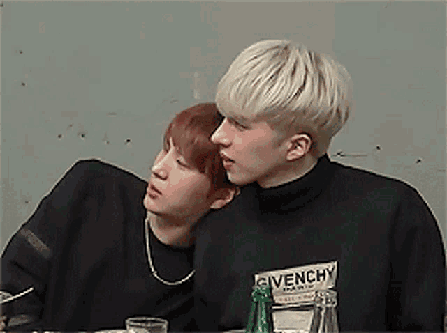 two young men are sitting at a table with one wearing a givenchy shirt