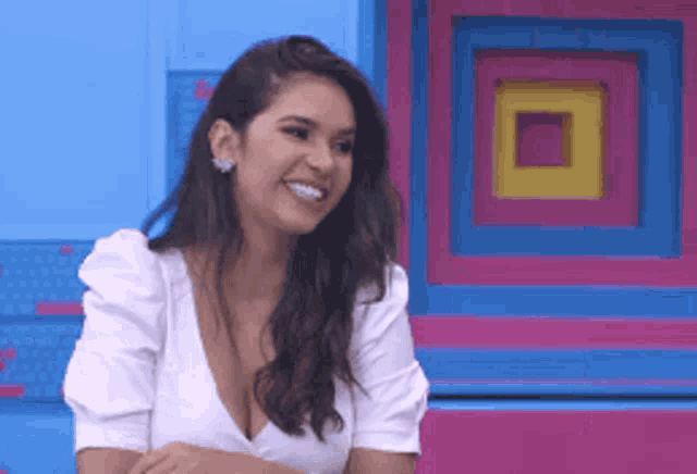 a woman in a white top is smiling in front of a colorful wall .