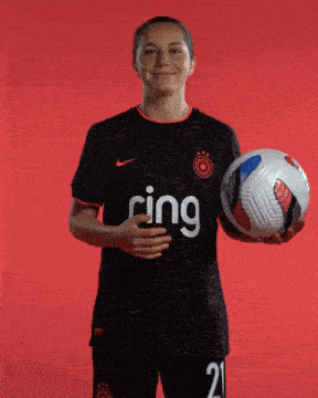 a woman in a ring jersey holds a soccer ball in her hand