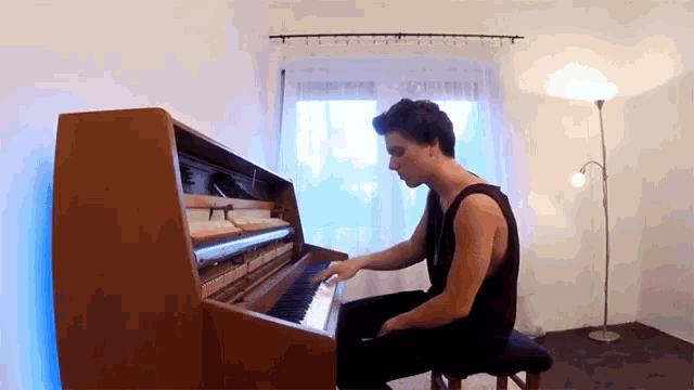 a man in a black tank top is playing a piano in a living room