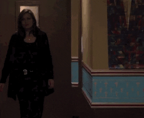 a man in a suit and tie is walking down a hallway with a gun in his hand .