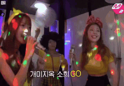 a group of girls are singing into microphones at a party and the words go are on the bottom of the screen .
