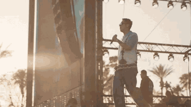 a man singing into a microphone on a stage with palm trees in the background