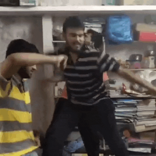 two men are dancing in a room with a lot of books on the shelf .