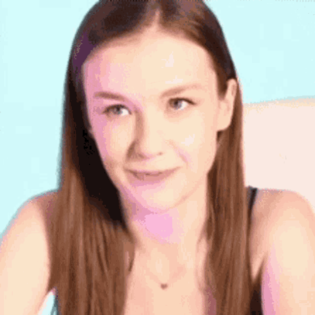 a woman with long brown hair is smiling and wearing a black tank top .
