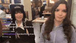 two girls are sitting at a table in a restaurant and one of them has a cat hat on