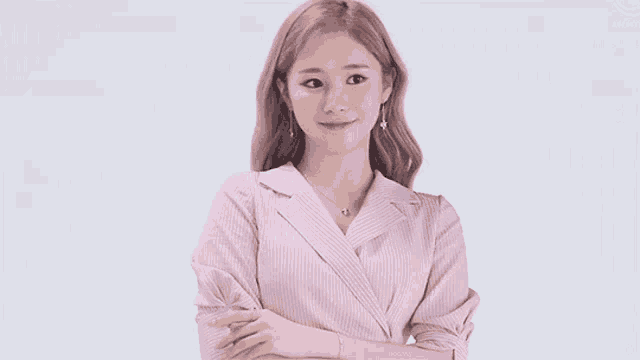 a woman wearing a pink striped shirt and earrings is standing with her arms crossed .