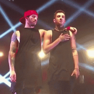two men are standing next to each other on a stage and one of them is holding his chest .