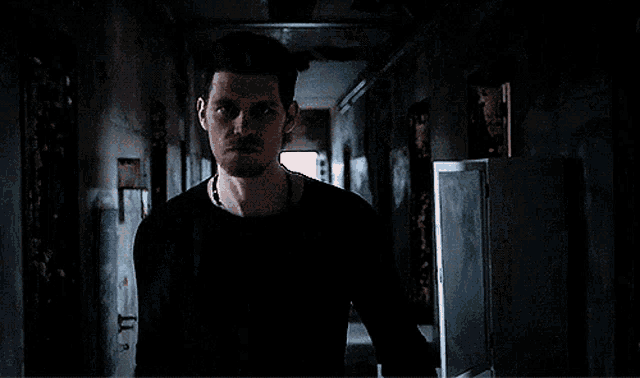 a man in a black shirt is standing in a dark hallway looking at the camera