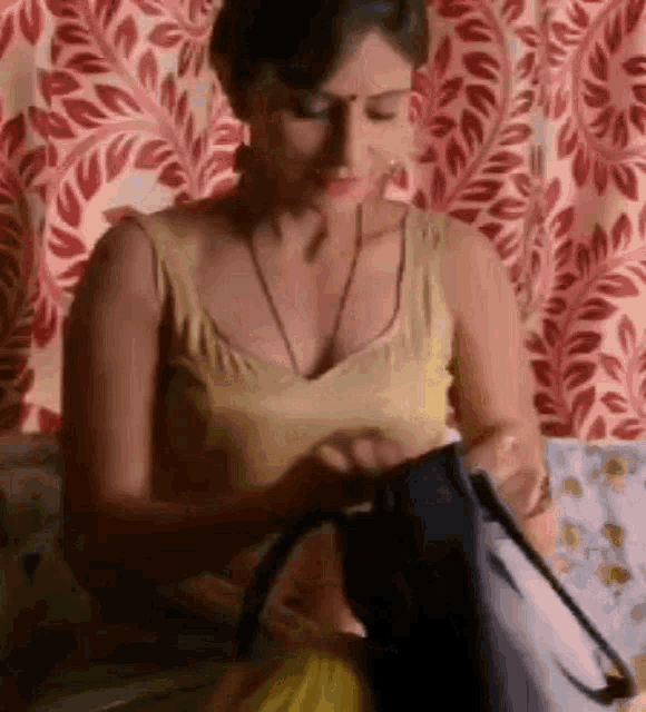 a woman in a yellow top is sitting on a bed holding a black bag .