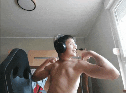 a shirtless young man wearing headphones flexes his muscles