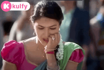 a woman in a pink top and green and blue saree is covering her nose with her hand .