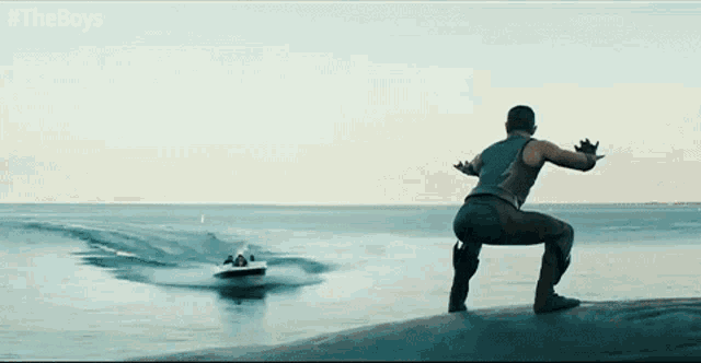 a man is squatting on a rock in front of a boat with #theboys written on it