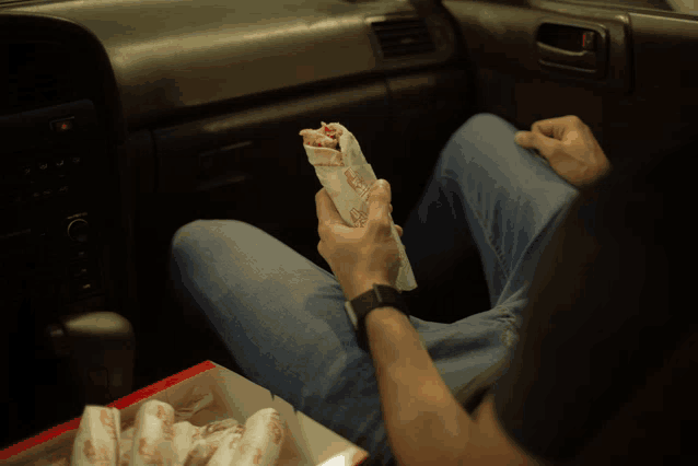 a man is sitting in a car holding a wrap that says ' chicken ' on it