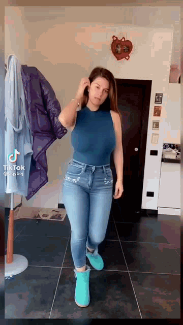 a woman in a blue tank top and jeans is standing on a tiled floor .