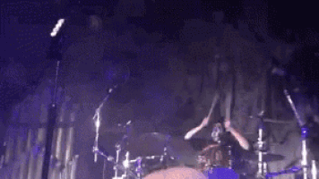 a man is playing drums on a stage with a microphone in the background .