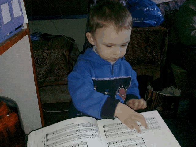 a young boy in a blue jacket is looking at a sheet music book