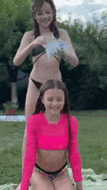 two young girls in bikinis are playing with water in the grass .