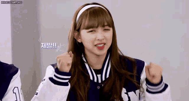 a girl wearing a baseball jacket and a headband is making a fist gesture .