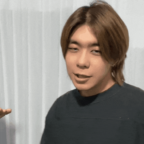 a young man with long brown hair is wearing a black shirt and making a funny face