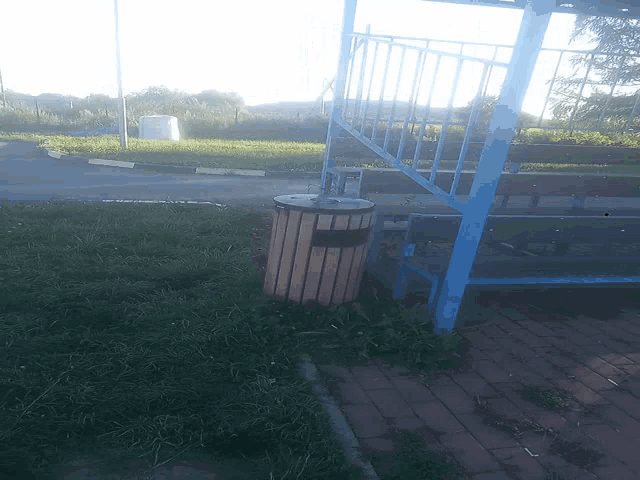 a wooden trash can sits in the grass next to a blue fence